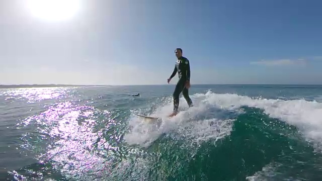 慢镜头，镜头光晕:快乐的男性冲浪者骑在波浪和跳进水里。