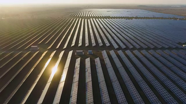 大面積的藍色光伏太陽能電池板在日落。陽光反射。鳥瞰圖。向前飛行。遠景。