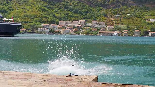 大丹犬沿着码头跑下来，跳进海水里溅起一大片水花