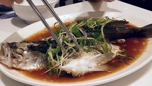 运动的女人吃清蒸鲈鱼与香草和蔬菜在餐厅供应的白盘