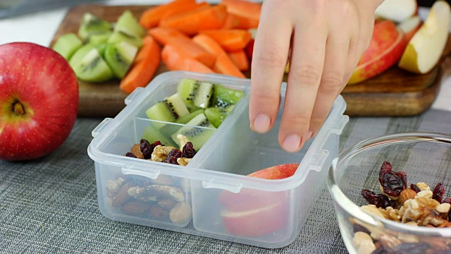 女人用手把健康的水果和坚果零食放进午餐盒里并关上