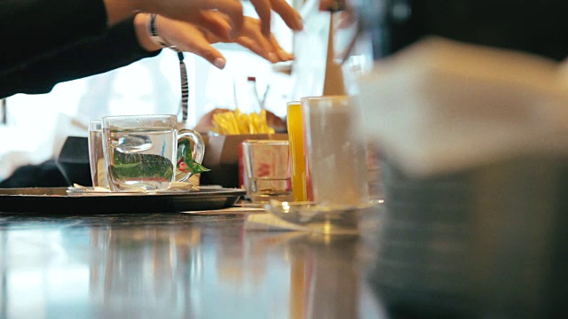 女服务员从咖啡馆的柜台上拿着盛有茶和果汁的玻璃杯