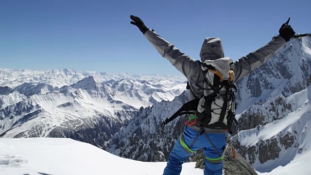 在阳光明媚的日子里，登山运动员成功登顶雪山。登山滑雪活动。滑雪者冬季在高山户外进行滑雪运动。后视图。慢动作60p 4k视频