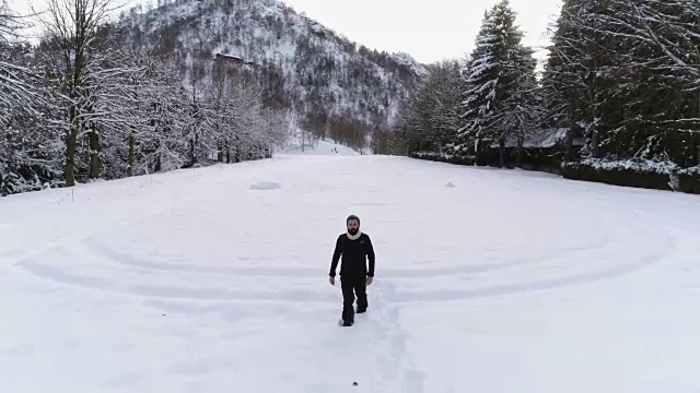 在冬季，在松林附近的雪地上，人们穿着雪鞋向后空中行走。欧洲阿尔卑斯山户外自然景观雪山。前面跟着徒步的人们。4 k无人机飞行