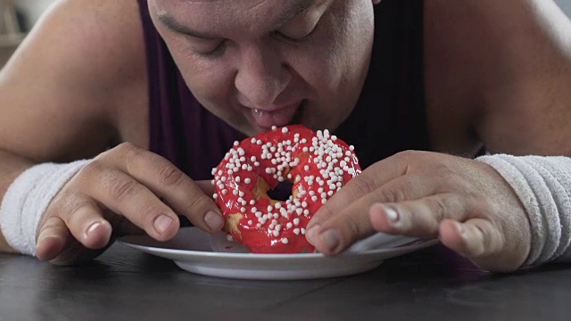 肥胖的人躺在地板上，带着食欲看着甜甜圈，肥胖