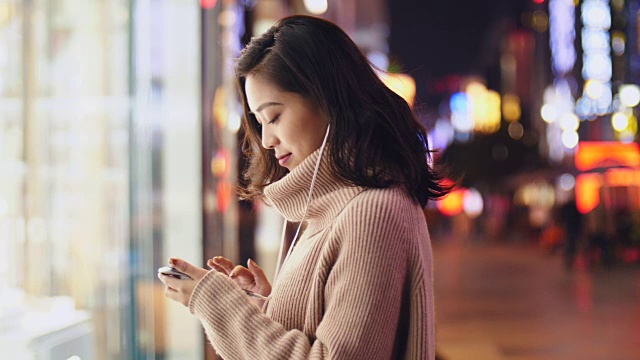 年輕的亞洲女人晚上在街上用智能手機