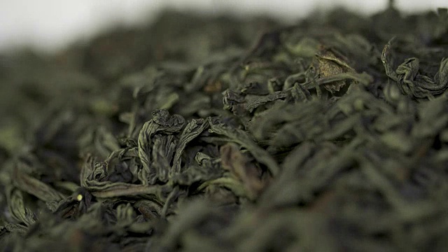 飘落的干绿茶叶子在白色的背景上。白色背景上的茶滴