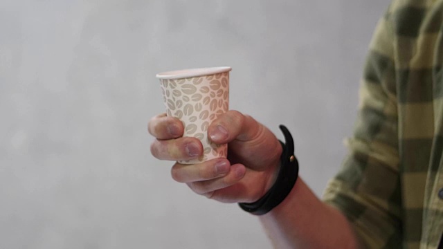男人拿着白色的杯子，然后它变成了纸杯的咖啡。一个男人拿着一个棕色的纸杯。拿着空杯子的男人，靠近点