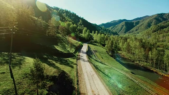 空中FHD全高清视图。在阳光明媚的夏日清晨，低空飞过山区乡村土路和草地。附近有绿树，阳光和山河