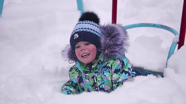 一个小孩在冬天的公园里玩雪。躺在白雪上微笑的婴儿。新鲜的空气里充满了乐趣和游戏。