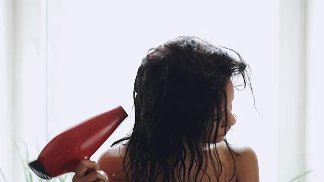 深色头发的女人用毛巾在家里用吹风机烘干头发