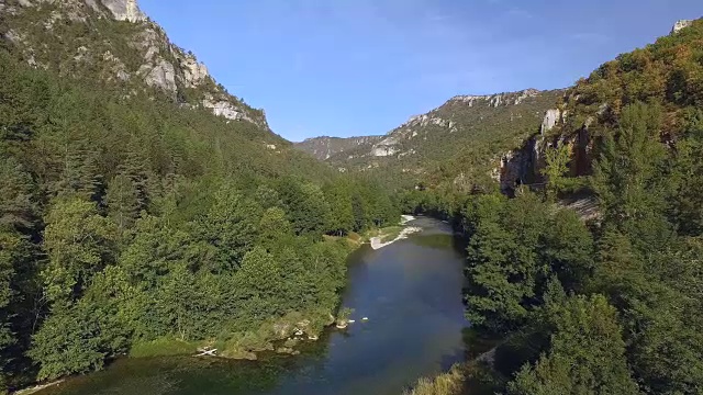 一条河流缓缓地流过森林覆盖的山丘和峭壁之间。阳光照亮了风景。