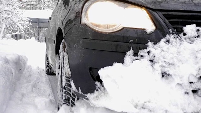 一辆黑色的汽车在一片白雪皑皑的森林里慢慢地行驶，密密麻麻的树木和树根在白雪皑皑的森林里。远足和旅行的概念，近60帧/秒