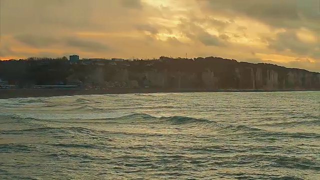 海浪的景象，诺曼底，迪耶普。多云的天气和日落在海岸。蔚蓝的海水和海滩上的泡沫。在法国北部度假。行动。实时视频，晚上。