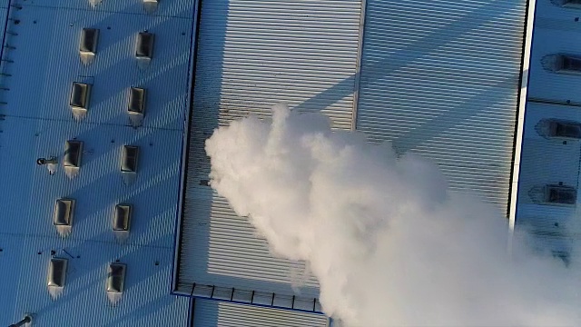 烟从工厂或工厂的屋顶上的管道排出，生产车间的屋顶上有一根管道，白色的浓烟从管道排出