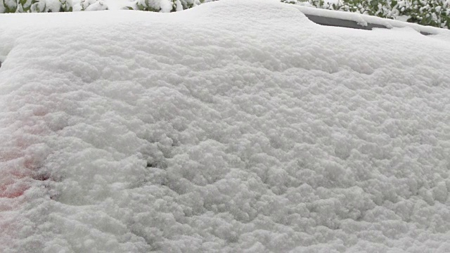 一辆被雪覆盖的汽车上的爱情告白——一名女子正在一辆被雪覆盖的汽车的后车窗上画一个心形