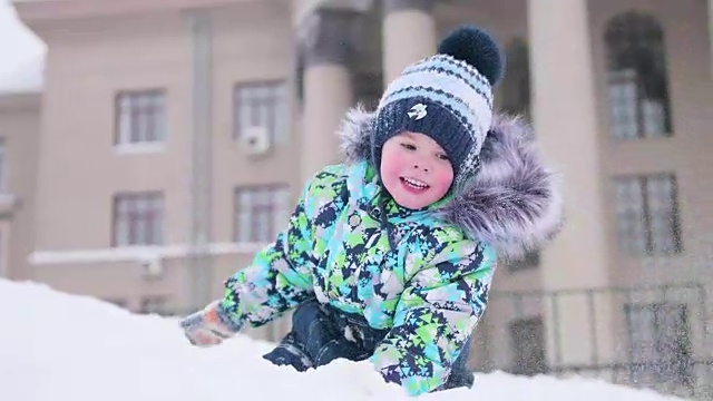 一个小孩在雪山上玩，扔雪，笑。阳光明媚的一天。新鲜的空气里充满了乐趣和游戏。