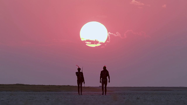 详情图-博茨瓦纳，两名圣布须曼人正穿过Makgadikgadi,pan，身后是夕阳西下的红色天空