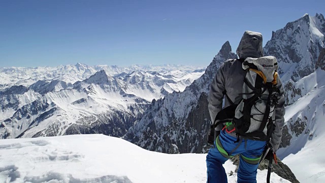 在阳光明媚的日子里，登山运动员成功登顶雪山。登山滑雪活动。滑雪者冬季在高山户外进行滑雪运动。后视图。慢动作60p全高清视频