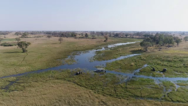 在奥卡万戈三角洲众多弯曲的水道之一的河岸上，一艘观光船的高空鸟瞰图看着大象进食