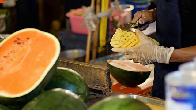 卖主正在用刀清理柜台后面的菠萝。亚洲的街头食品。泰国