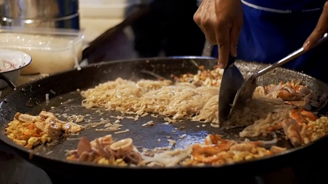 亚洲的街头食品。海鲜、米粉搭配鸡蛋在大煎锅上煮。缓慢的运动。泰国