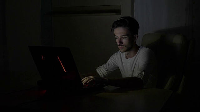 年轻的男学生晚上坐在家里的书桌上用笔记本电脑在线思考和解决数学问题