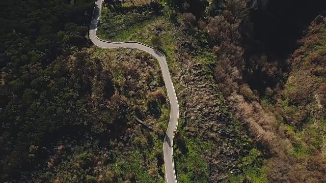 无人机飞过狭窄的山路。鸟瞰图森林车道开放，通过汽车和建筑物。4 k