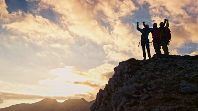 三个登山者在日落时分在山顶击掌