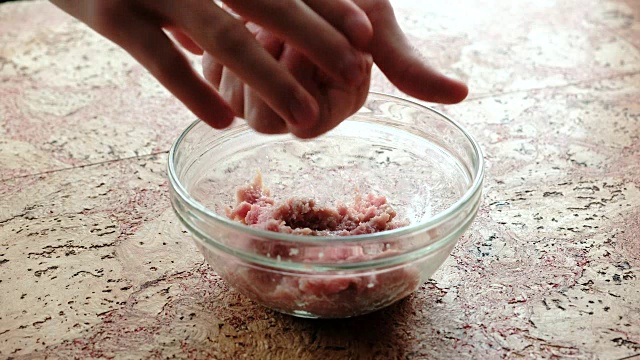 男子双手的特写使肉糜变成了肉片。厨房桌上的透明盘子。