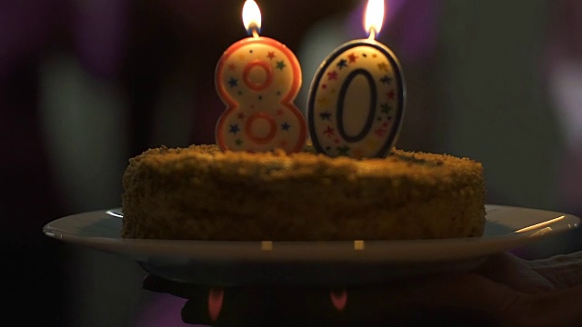 朋友们向面带微笑的老夫人赠送生日蛋糕，庆祝气氛热烈