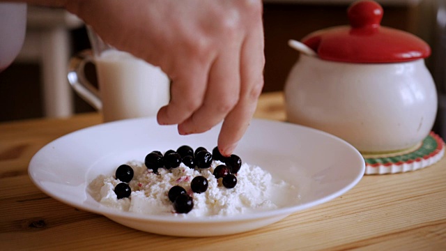 这个男人正在用醋栗浆果做一道美味的凝乳甜点。厨师制作甜点的双手。白软干酪和新鲜浆果。缓慢的运动。
