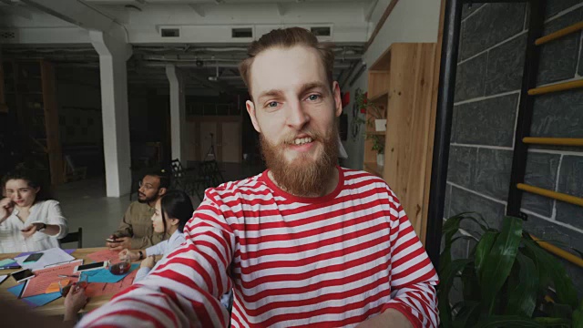 特写的潮人拿着智能手机，有实时视频通话，而他的同事在现代办公室工作