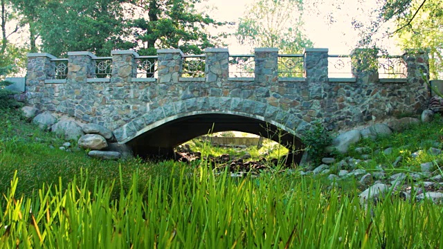 在一个晴朗的夏日，公园里的石桥在一条干涸的小溪上