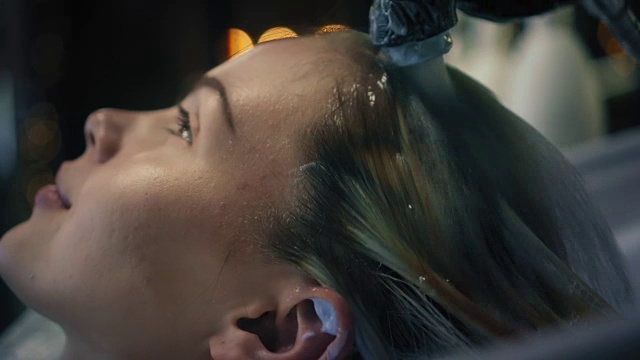 发型师戴着黑手套，在发廊的水槽里仔细地洗掉女人长长的金发上的染发剂