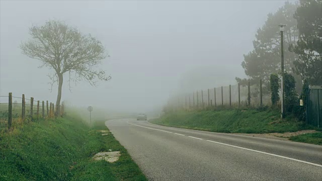 在一个雾天，汽车行驶在乡间柏油路上穿过田野的时间流逝