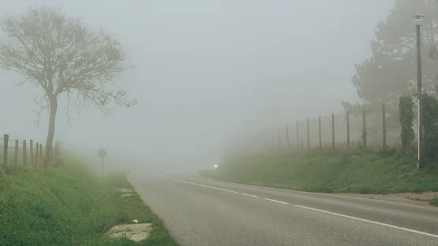 在雾天，汽车行驶在乡间的柏油路上，穿过田野。时间流逝缩小