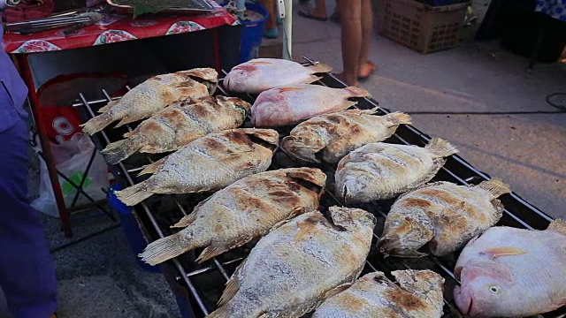 在泰国的夜市上，一名男子在街头贩卖食物，烹饪海鱼