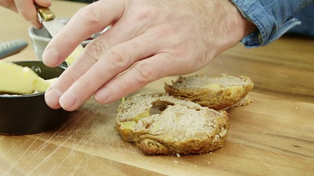 男人的手在切烤饼和用刀抹黄油