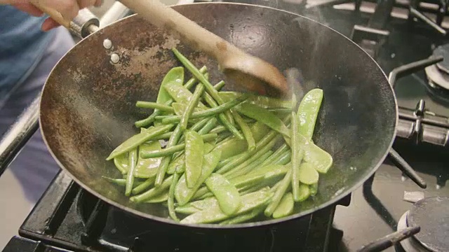 一名男子在厨房炉子上的锅里炒四季豆