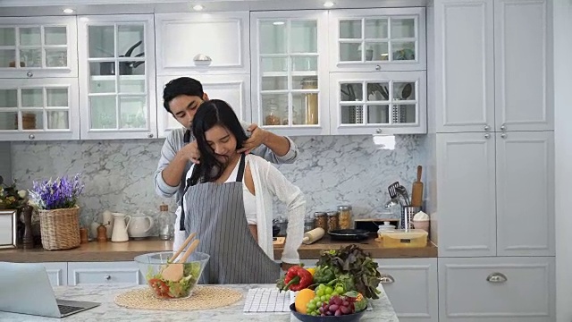 年轻的丈夫在做饭前为他怀孕的妻子系上围裙