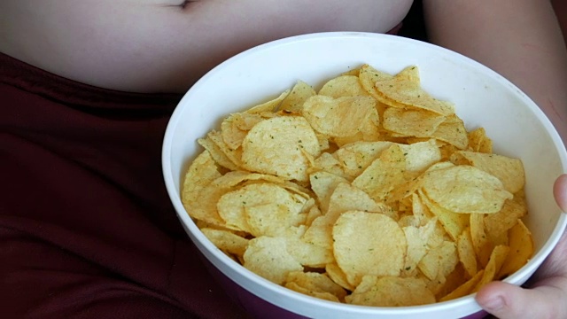 胖男孩在吃薯片。孩子腹部脂肪褶皱。不健康食品，快餐