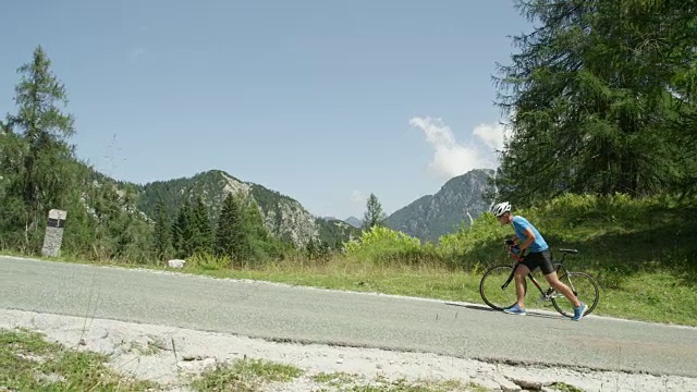 慢镜头:被陡峭的山路打败，骑自行车的人沿着自行车走。