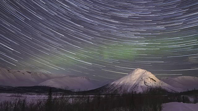 累积时间流逝的夜晚星空与星迹和绿色北极光在雪山冬夜。