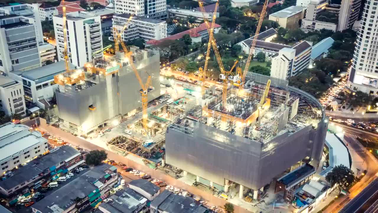 延时拍摄的建筑工地，在夜晚有城市交通的灯光轨迹，俯视图。先进的建筑技术，繁忙的地铁市中心城市景观，或发展中的工业国家概念