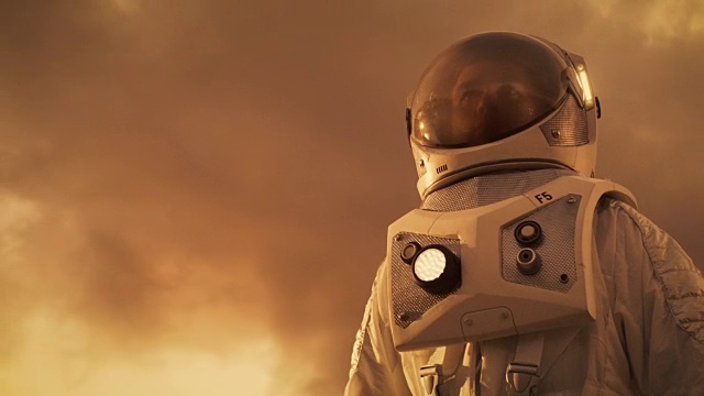 詳情圖-低角度拍攝的勇敢宇航員穿著宇航服環(huán)顧外星球。類似火星的紅色和橙色星球。先進技術，太空旅行，殖民概念。