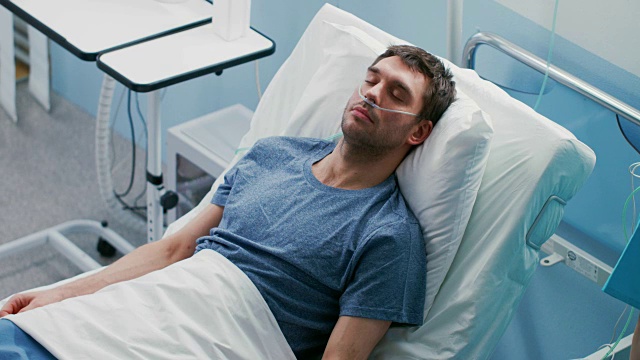 在医院生病的男性病人睡在床上，他戴着鼻导管。护士进来检查他的掉落计数器，增加止痛剂量。