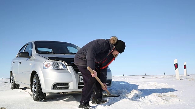 司机用铲子把汽车从雪中挖出来。