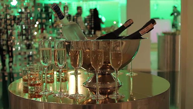 自助餐桌上放着一杯香槟和葡萄酒，桶里装着一瓶香槟或葡萄酒，背景是人们在跳舞，模糊的剪影