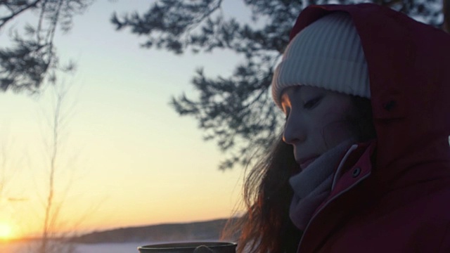 日落时分，在白雪覆盖的冬日森林里，女游客正在用保温瓶喝茶